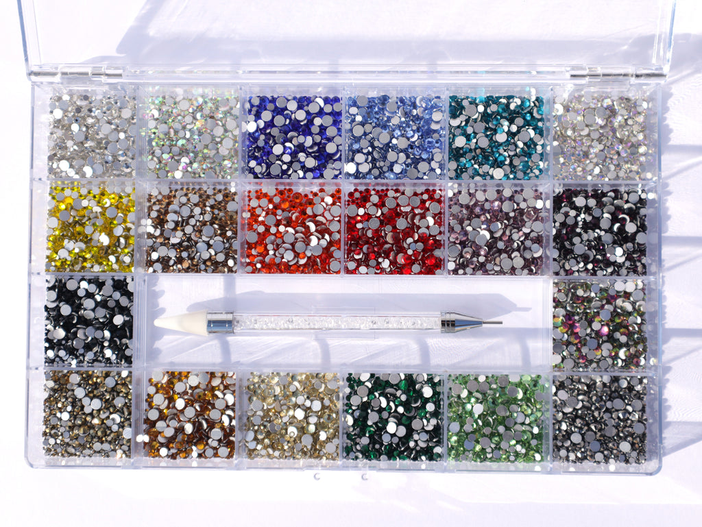 Assorted colorful rhinestones in a clear organizer with a tool on a white background